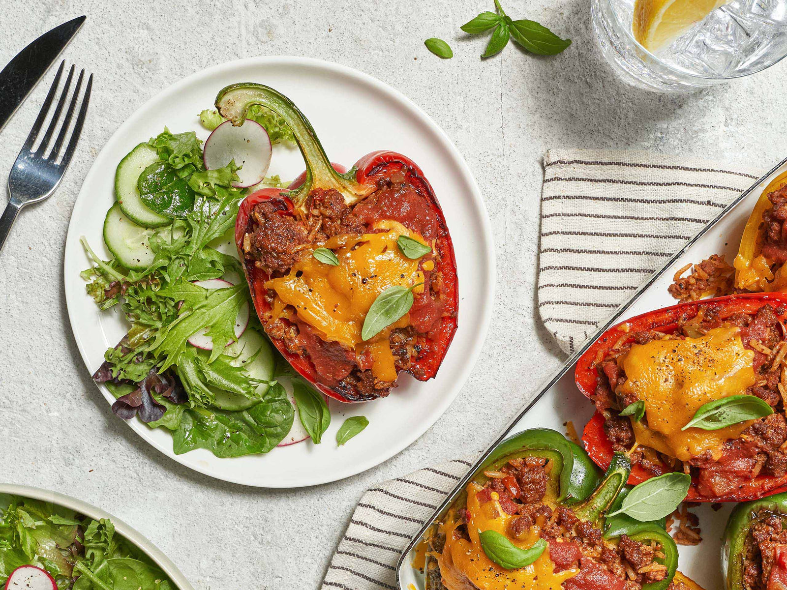 Bell Pepper Stuffed with Beef and Cheese, Cut Crosswise with Side Salad on White Plate with More Stuffed Peppers on the Side